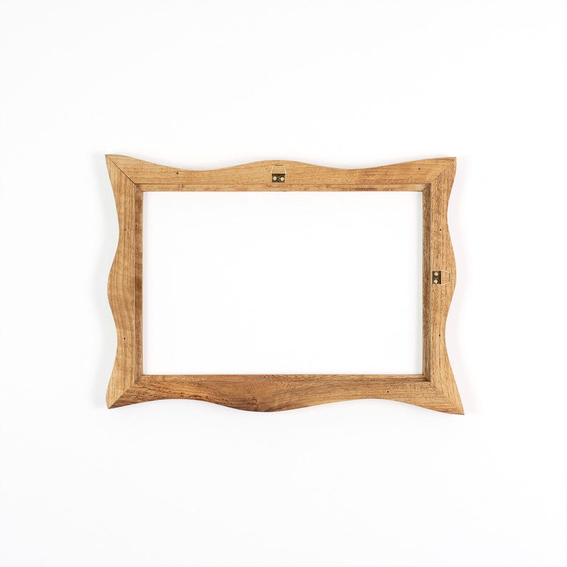 Puede incluir: Un marco de fotos de madera marr&oacute;n claro con un borde ondulado e irregular. El marco tiene una abertura rectangular. Se ve el herraje met&aacute;lico para colgar en la parte posterior.