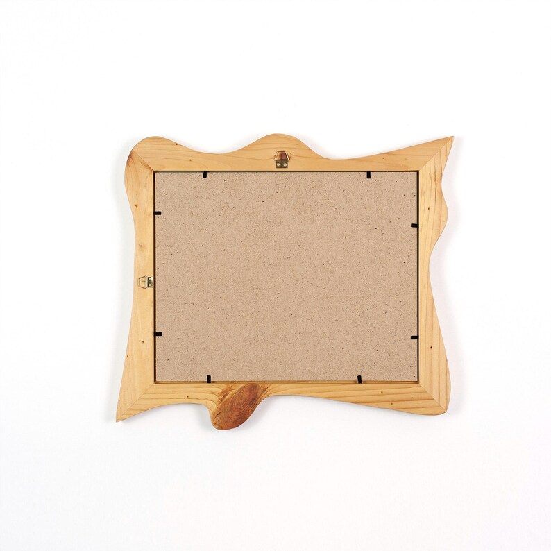 May include: A rectangular picture frame with a natural light wood finish and an irregular, live-edge border. The back of the frame is covered with a flat, tan-colored fiberboard panel secured by small metal clips, featuring a metal hanging bracket.