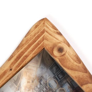 May include: A triangular wooden picture frame with a natural light brown finish, featuring visible wood grain patterns and knots. The frame has a mitred corner joint at the top peak and contains a clear glass pane protecting an internal image.