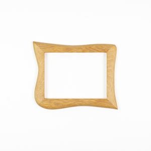May include: A rectangular wooden picture frame with a light brown natural wood grain finish. The frame features a distinct wavy, organic contour along its outer edges, while the inner opening remains a standard rectangular shape for display.
