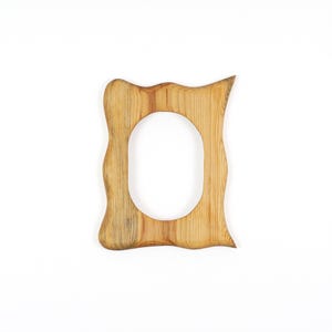 May include: A wooden picture frame with a natural finish. The frame has an oval opening and a wavy, organic shape. The wood grain is visible, adding texture to the design. The frame is set against a white background.