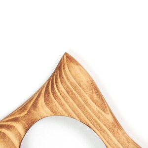 Pode incluir: Close-up de um objeto de madeira com formato triangular e uma abertura arredondada. A madeira &eacute; marrom claro com padr&otilde;es de gr&atilde;o vis&iacute;veis. O objeto parece fazer parte de uma estrutura maior, possivelmente um elemento decorativo ou um m&oacute;vel.