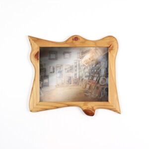 Peut inclure: Un cadre photo rectangulaire fabriqu&eacute; en bois naturel clair avec une bordure irr&eacute;guli&egrave;re et organique. Le cadre pr&eacute;sente des motifs de grain de bois et des n&oelig;uds visibles, entourant une impression repr&eacute;sentant une sc&egrave;ne d'int&eacute;rieur.