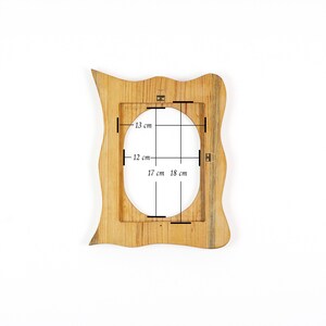 May include: A wooden picture frame with a unique, wavy edge design. The frame has an oval opening with dimensions of 13 cm x 12 cm (5.1 in x 4.7 in) and 17 cm x 18 cm (6.7 in x 7.1 in). The frame is made of light brown wood.
