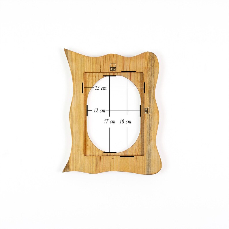 May include: A wooden picture frame with a unique, wavy edge design. The frame has an oval opening with dimensions of 13 cm x 12 cm (5.1 in x 4.7 in) and 17 cm x 18 cm (6.7 in x 7.1 in). The frame is made of light brown wood.
