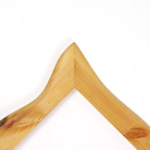 May include: A light brown wooden clothes hanger featuring a prominent natural wood grain pattern with visible knots. The hanger has a smooth, curved shape that comes to a central point at the top, showcasing the organic texture of the wood material.