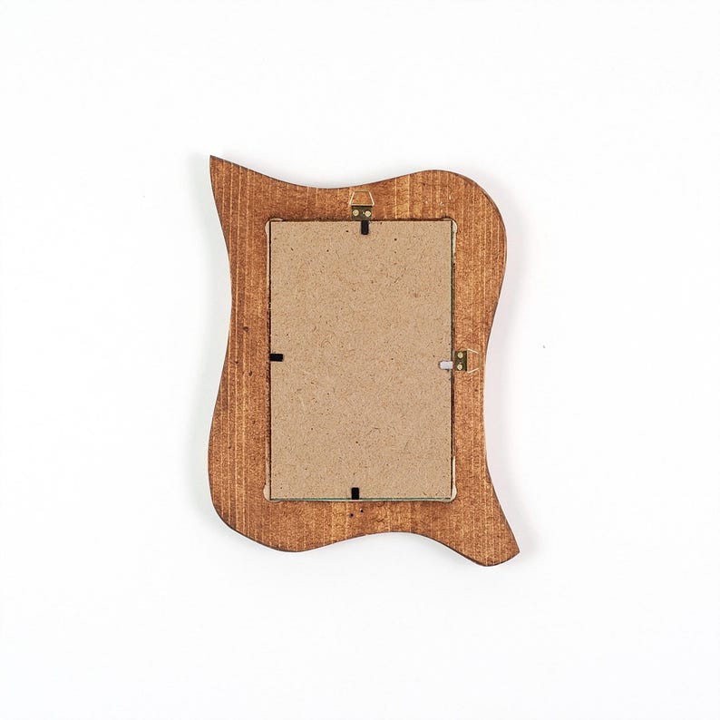 May include: A wooden picture frame with a distinctive, wavy edge design. The frame is stained a warm brown colour and has a cardboard backing. It features metal hanging hardware. The overall shape is rectangular with curved edges.