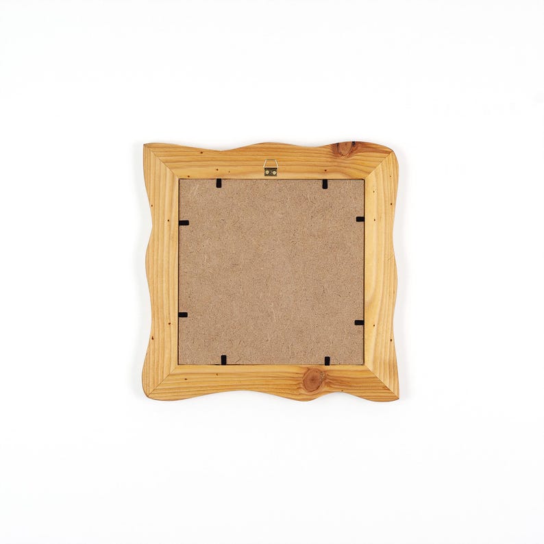 Puede incluir: Un marco de fotos cuadrado de madera con un acabado natural en marr&oacute;n claro y bordes ondulados y org&aacute;nicos. La parte posterior del marco presenta un panel de fibra de color beige, asegurado con clips met&aacute;licos y un peque&ntilde;o gancho de metal dorado.
