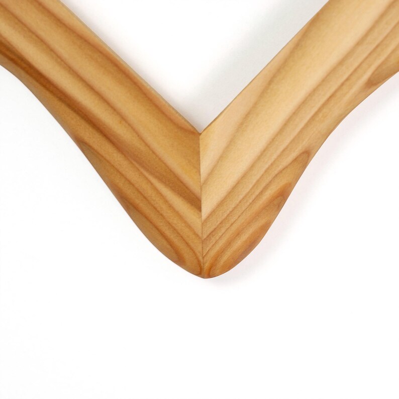 Puede incluir: Una secci&oacute;n de esquina de marco de fotos de madera de color marr&oacute;n claro con una uni&oacute;n a inglete. La madera muestra un patr&oacute;n de veta natural con bordes lisos y curvos y un acabado pulido, formando un &aacute;ngulo en V que resalta la uni&oacute;n.