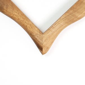 Puede incluir: Primer plano de una esquina de un marco de madera. El marco es de madera marr&oacute;n claro con veta natural. El marco tiene forma de V, con los dos lados uni&eacute;ndose en &aacute;ngulo agudo. El fondo es blanco.