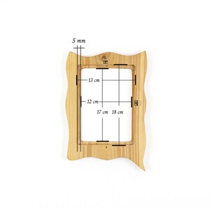 May include: A light-colored wooden picture frame with a wavy, irregular border. The frame's inner dimensions are 17 cm by 18 cm, and 12 cm by 13 cm. The frame is 5 mm thick and has a hanging mechanism on the back.