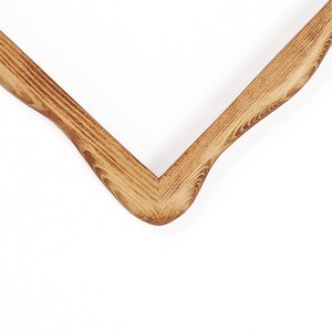 May include: A V-shaped wooden frame corner featuring a natural light brown wood grain pattern. The two segments meet at a sharp, mitered angle, showcasing the distinct texture and organic lines of the wood grain throughout the entire surface.