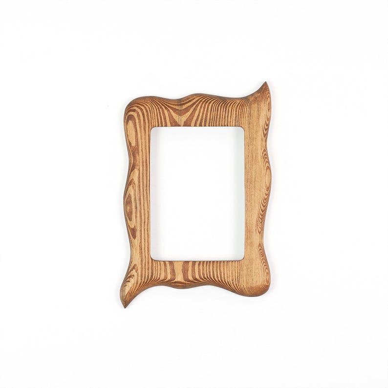 Peut inclure: Un cadre photo rectangulaire en bois pr&eacute;sentant un motif de grain de bois naturel aux tons marron clair et fonc&eacute;. Le cadre poss&egrave;de un bord ext&eacute;rieur irr&eacute;gulier, ondul&eacute; et organique avec une finition lisse, entourant une ouverture centrale.