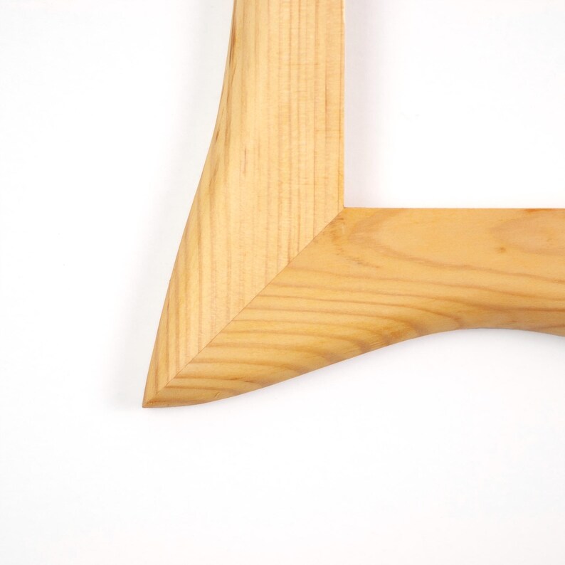 May include: A light-colored wooden picture frame corner featuring a mitered joint. The natural wood grain is visible throughout the surface, showcasing a smooth, polished finish with a distinct curved inner edge and a sharp, angled outer corner.