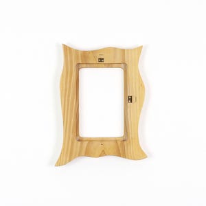 May include: A light-colored wooden picture frame with a wavy, organic outer edge and a rectangular inner opening. The frame features visible wood grain patterns and includes two small metal hanging brackets attached to the back side.