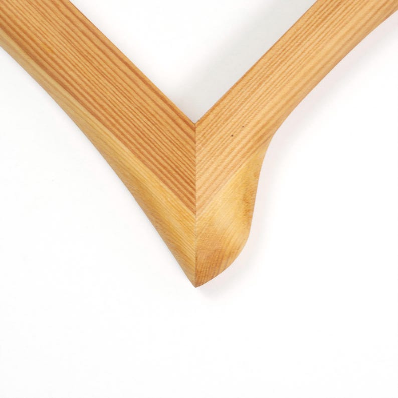 Puede incluir: Primer plano de una esquina de un marco de fotos de madera. El marco es de madera clara con vetas visibles. La esquina tiene un dise&ntilde;o suave y curvado, con una junta en forma de V.