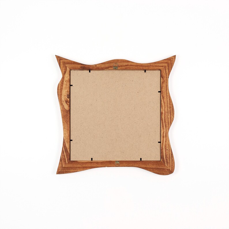 May include: A square wooden picture frame with a wavy, decorative edge. The frame is made of light brown wood and has a cardboard backing. The frame is designed to hold a photograph or artwork.