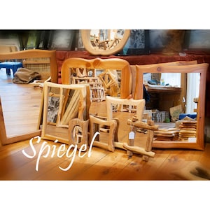 Peut inclure: Une collection de miroirs encadr&eacute;s en bois de diff&eacute;rentes tailles et formes, dont des mod&egrave;les rectangulaires, carr&eacute;s et ovales. Les miroirs sont expos&eacute;s sur un sol en bois, avec le mot "Spiegel" en &eacute;criture blanche.
