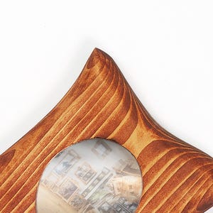 May include: A star-shaped wooden picture frame with a warm brown finish and visible wood grain patterns. The frame features a circular center cutout that displays a blurred interior scene with multiple small framed images on a wall.