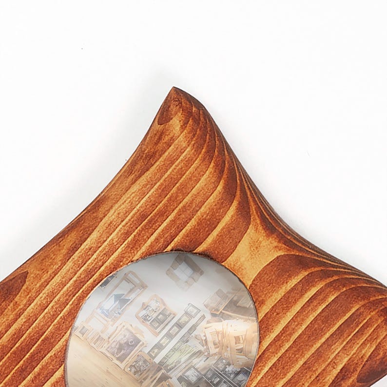 May include: A star-shaped wooden picture frame with a warm brown finish and visible wood grain patterns. The frame features a circular center cutout that displays a blurred interior scene with multiple small framed images on a wall.