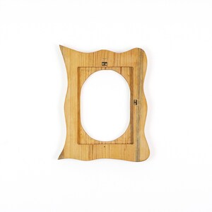May include: A wooden picture frame with an oval opening. The frame has a unique, wavy shape and is made of light-colored wood. It has a natural wood grain pattern and metal hanging hardware on the back.
