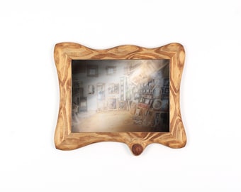 Könnte beinhalten: Ein hellbrauner Holzbilderrahmen mit einem einzigartigen, wellenförmigen Design. Der Rahmen weist dunklere Maserungsmuster auf. Am unteren Rand befindet sich ein kleines, rundes Holzdetail. Das Bild zeigt einen Raum mit Kunst.