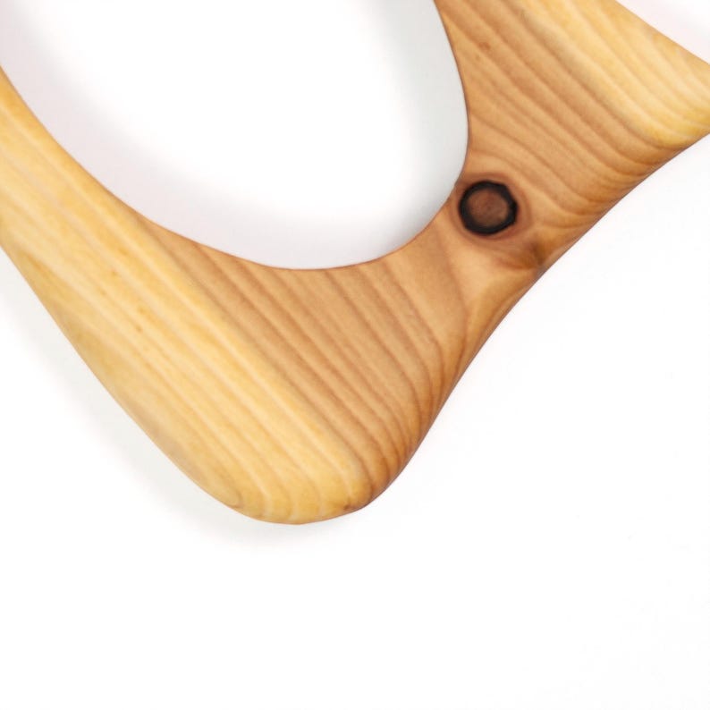 May include: Close-up of a wooden boomerang with a natural wood grain finish. The boomerang has a curved shape with rounded edges and a knot detail. The wood is light brown with darker brown accents.