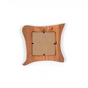 K&ouml;nnte beinhalten: Ein Bilderrahmen aus Holz mit gewelltem, unregelm&auml;&szlig;igem Au&szlig;enrand und einer nat&uuml;rlichen braunen Holzmaserung. Die R&uuml;ckseite des Rahmens verf&uuml;gt &uuml;ber eine quadratische Kartonr&uuml;ckwand mit Metallklammern und einen kleinen messingfarbenen Aufh&auml;nger.