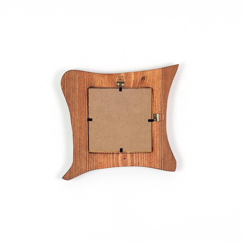K&ouml;nnte beinhalten: Ein Bilderrahmen aus Holz mit gewelltem, unregelm&auml;&szlig;igem Au&szlig;enrand und einer nat&uuml;rlichen braunen Holzmaserung. Die R&uuml;ckseite des Rahmens verf&uuml;gt &uuml;ber eine quadratische Kartonr&uuml;ckwand mit Metallklammern und einen kleinen messingfarbenen Aufh&auml;nger.