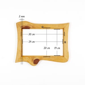 Puede incluir: Un marco de fotos de madera de color marr&oacute;n claro con un borde natural y veta visible. El marco cuenta con herrajes met&aacute;licos para colgar en la parte posterior. Las anotaciones t&eacute;cnicas indican un grosor de 5 mm y medidas internas de 30 cm por 20 cm.