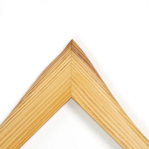 K&ouml;nnte beinhalten: Ein Eckst&uuml;ck eines Bilderrahmens aus hellem Holz mit sichtbarer nat&uuml;rlicher Maserung. Der Rahmen weist an der oberen Spitze eine Gehrungsverbindung auf, die einen scharfen Winkel bildet, an dem die beiden Holzsegmente sauber und pr&auml;zise aufeinandertreffen.