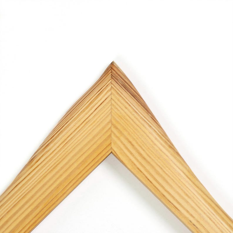 K&ouml;nnte beinhalten: Ein Eckst&uuml;ck eines Bilderrahmens aus hellem Holz mit sichtbarer nat&uuml;rlicher Maserung. Der Rahmen weist an der oberen Spitze eine Gehrungsverbindung auf, die einen scharfen Winkel bildet, an dem die beiden Holzsegmente sauber und pr&auml;zise aufeinandertreffen.