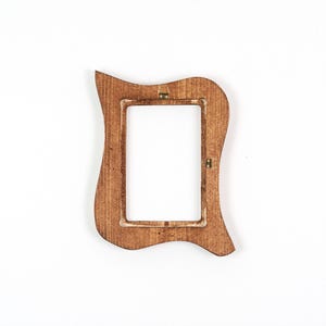 May include: A decorative wooden picture frame with an unusual, curved shape. The frame is a warm brown colour and has a rectangular aperture for a photograph. The back of the frame has metal fixings for hanging. It is set against a white background.