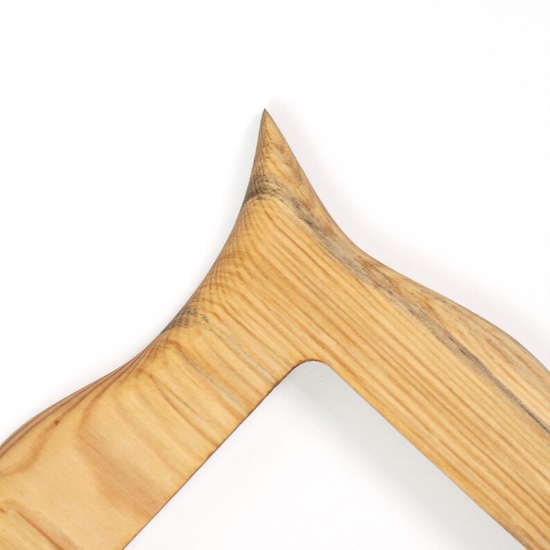 Pu&ograve; includere: Primo piano di un oggetto in legno con una punta e un design angolare curvo. La venatura del legno &egrave; visibile, con un colore marrone chiaro e striature pi&ugrave; scure. L'oggetto sembra far parte di una struttura pi&ugrave; grande.