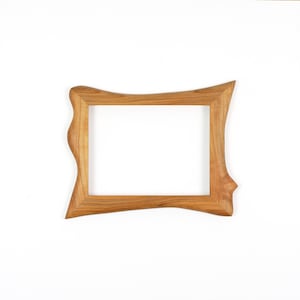 Puede incluir: Un marco de fotos rectangular hecho de madera de color marr&oacute;n claro con un patr&oacute;n de grano natural visible. El marco presenta un dise&ntilde;o exterior irregular y ondulado, manteniendo una abertura rectangular est&aacute;ndar para exhibir fotos o arte.