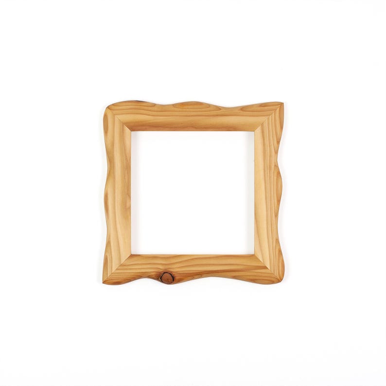 Puede incluir: Un marco de fotos cuadrado de madera en color tostado claro con patrones de veta de madera natural visibles. El marco tiene un borde exterior ondulado y org&aacute;nico distintivo y un borde interior liso, con un peque&ntilde;o nudo en la parte inferior.