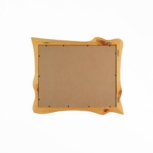 K&ouml;nnte beinhalten: Ein hellfarbiger Holzbilderrahmen mit einem einzigartigen, wellenf&ouml;rmigen Design. Der Rahmen hat eine nat&uuml;rliche Holzmaserung und eine braune R&uuml;ckseite. Der Rahmen ist mit Metallbeschl&auml;gen auf der R&uuml;ckseite zum Aufh&auml;ngen bereit.