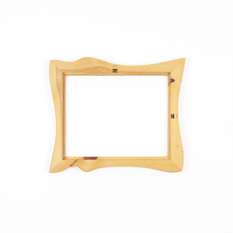 May include: A rectangular wooden picture frame with a natural light brown finish and visible wood grain. The frame features an irregular, wavy outer edge and includes two small metal hanging brackets attached to the inner wooden border.