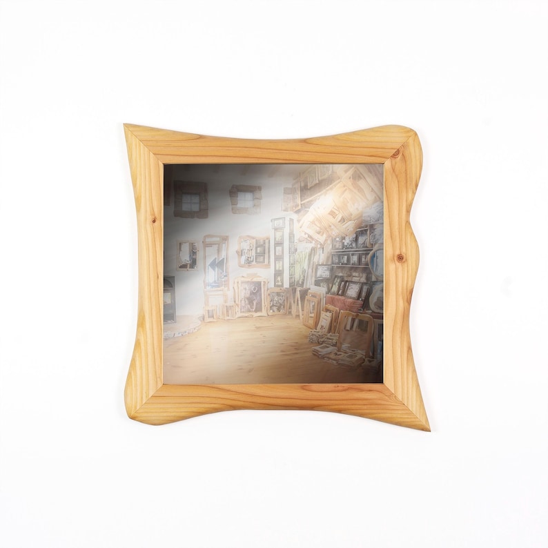 Peut inclure: Un miroir carr&eacute; dot&eacute; d'un cadre en bois clair naturel au design ondul&eacute; et irr&eacute;gulier. La surface r&eacute;fl&eacute;chissante montre une vue int&eacute;rieure d&eacute;form&eacute;e d'une pi&egrave;ce remplie de diverses &oelig;uvres d'art encadr&eacute;es et de meubles en bois.
