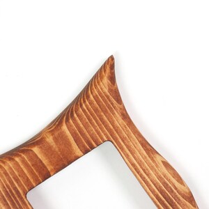 Peut inclure: Une section d'un objet en bois pr&eacute;sentant un coin pointu pro&eacute;minent et un bord incurv&eacute; lisse. La surface affiche un motif de grain de bois brun distinct avec des tons clairs et fonc&eacute;s vari&eacute;s, soulignant la texture naturelle du mat&eacute;riau.