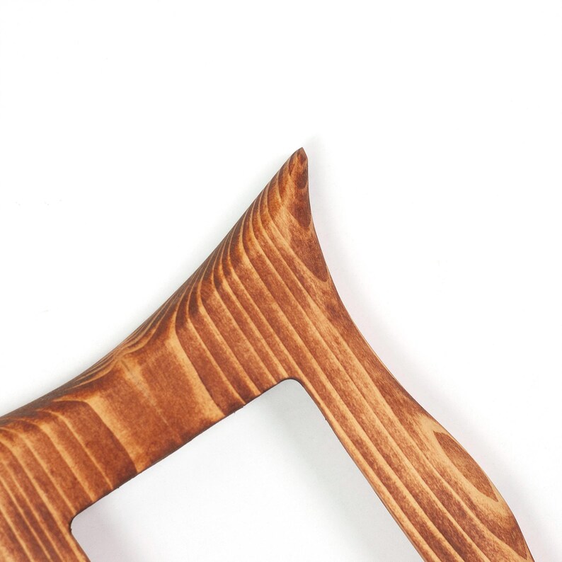 Peut inclure: Une section d'un objet en bois pr&eacute;sentant un coin pointu pro&eacute;minent et un bord incurv&eacute; lisse. La surface affiche un motif de grain de bois brun distinct avec des tons clairs et fonc&eacute;s vari&eacute;s, soulignant la texture naturelle du mat&eacute;riau.