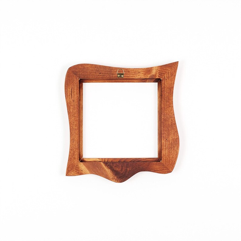 May include: A square wooden picture frame with a decorative, wavy edge. The frame is a warm brown colour and has a brass hanger on the back. The frame is empty, with a white background.