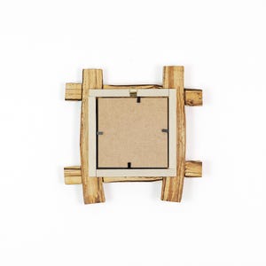 May include: A square picture frame with a natural wood grain finish, featuring a rustic overlapping log design. The back of the frame is made of light brown fibreboard, secured with metal clips, and includes a gold-coloured metal hanging bracket.