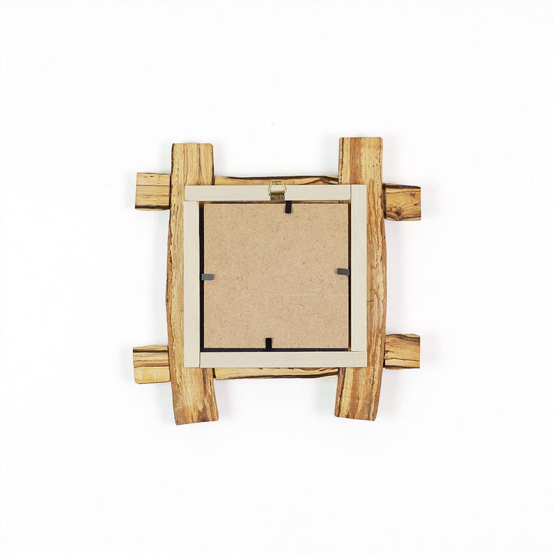 May include: A square picture frame with a natural wood grain finish, featuring a rustic overlapping log design. The back of the frame is made of light brown fibreboard, secured with metal clips, and includes a gold-coloured metal hanging bracket.