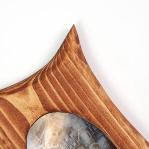 K&ouml;nnte beinhalten: Ein Bilderrahmen aus Holz mit einer spitzen, dreieckigen Ecke und einer glatten, polierten Oberfl&auml;che. Das Holz weist eine markante, dunkelbraune Maserung auf, die dem scharfen Winkel des Rahmens folgt und eine runde &Ouml;ffnung umschlie&szlig;t.