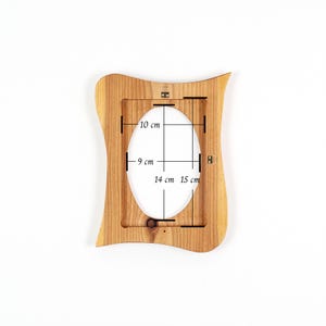 May include: A wooden picture frame with an oval opening. The frame is light brown and has a wavy, decorative edge. The opening dimensions are 9 cm x 14 cm, and the overall frame dimensions are 10 cm x 15 cm.