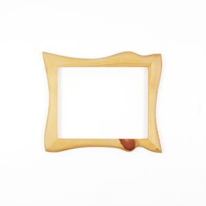 May include: A rectangular wooden picture frame with a light tan natural wood grain finish. The frame features an irregular, wavy outer edge design and a prominent dark brown circular wood knot detail on the bottom right side of the frame.