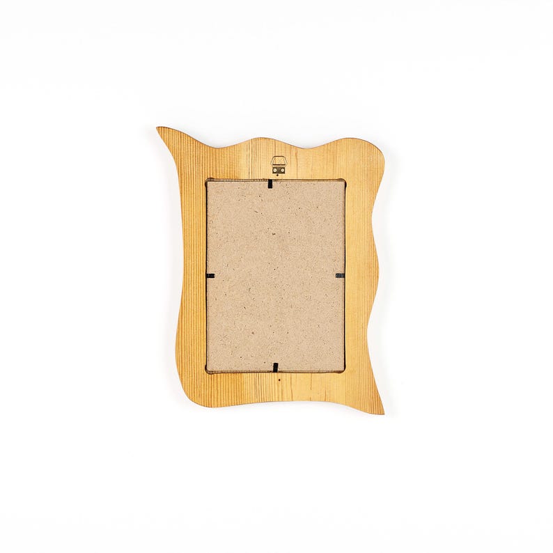 May include: A light brown wooden picture frame with a wavy, organic shape. The back of the frame is visible, showing a cardboard insert and a small metal hanger. The frame has a natural wood grain texture.