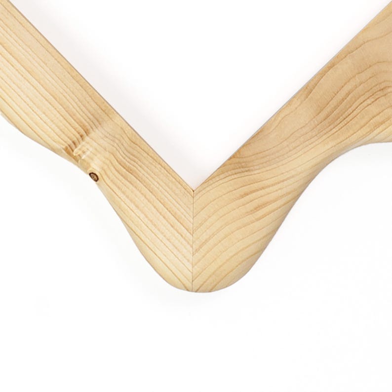 Puede incluir: Una percha de madera de color claro con un dise&ntilde;o en forma de V. La veta natural de la madera es claramente visible en toda la superficie, mostrando la textura org&aacute;nica y los tonos bronceados claros del material en la uni&oacute;n central.