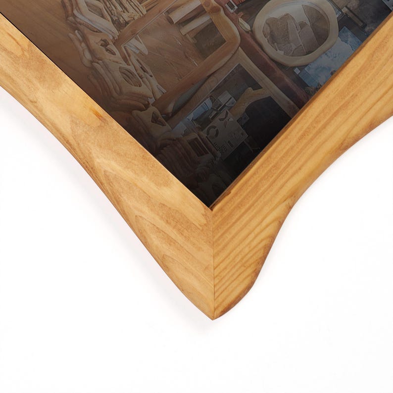 May include: A light-coloured wooden picture frame with a distinctive, curved design. The frame has a natural wood grain finish and a dark, reflective surface inside, possibly holding a photograph or artwork. The frame's edges are rounded.